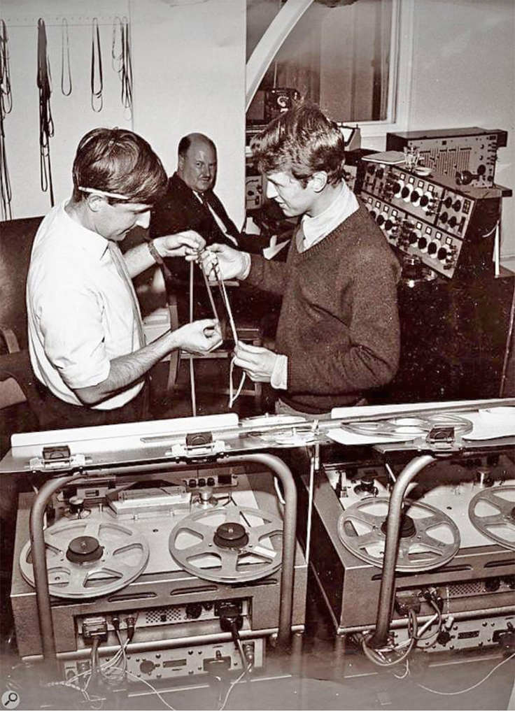 Dick Mills and Brian Hodgson compare the lengths of two sections of tape; watching is Desmond Briscoe. BBC Radiophonic Workshop 1968